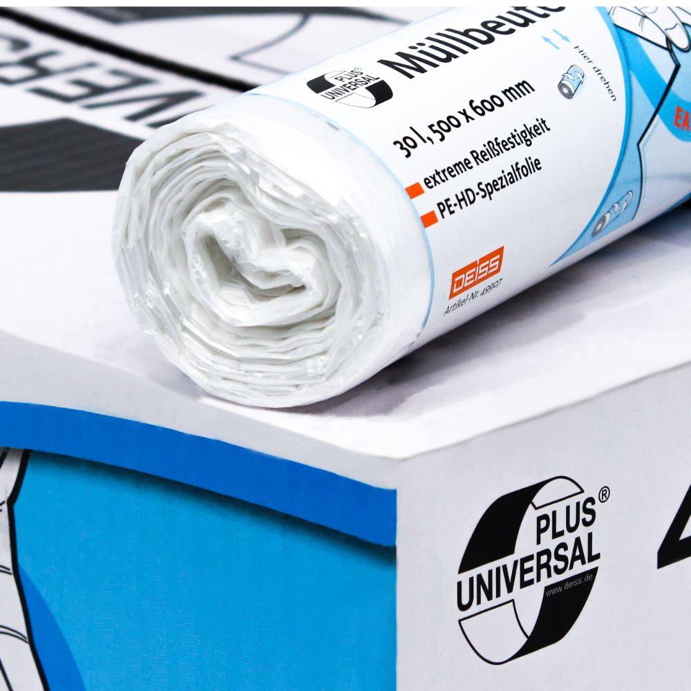 Eine Rolle DEISS Universal Plus® Müllbeutel, 30 Liter, von EMIL DEISS KG (GmbH + Co.) mit blauer und oranger Beschriftung liegt auf einem Karton. Der Text enthält „Müllbeutel“ sowie Angaben zur HDPE-Spezialfolie, den Abmessungen und dem Material. Im Hintergrund ist eine weitere Rolle teilweise sichtbar.