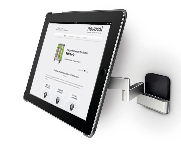 Eine Novocal iPad-Halterung Variante 1 für 7-12 Zoll Tablets, schwenkbar bis zu 180°, ist auf einer weißen Fläche montiert und hält ein Tablet, das die Novocal Website mit Produktinformationen und Navigation anzeigt.