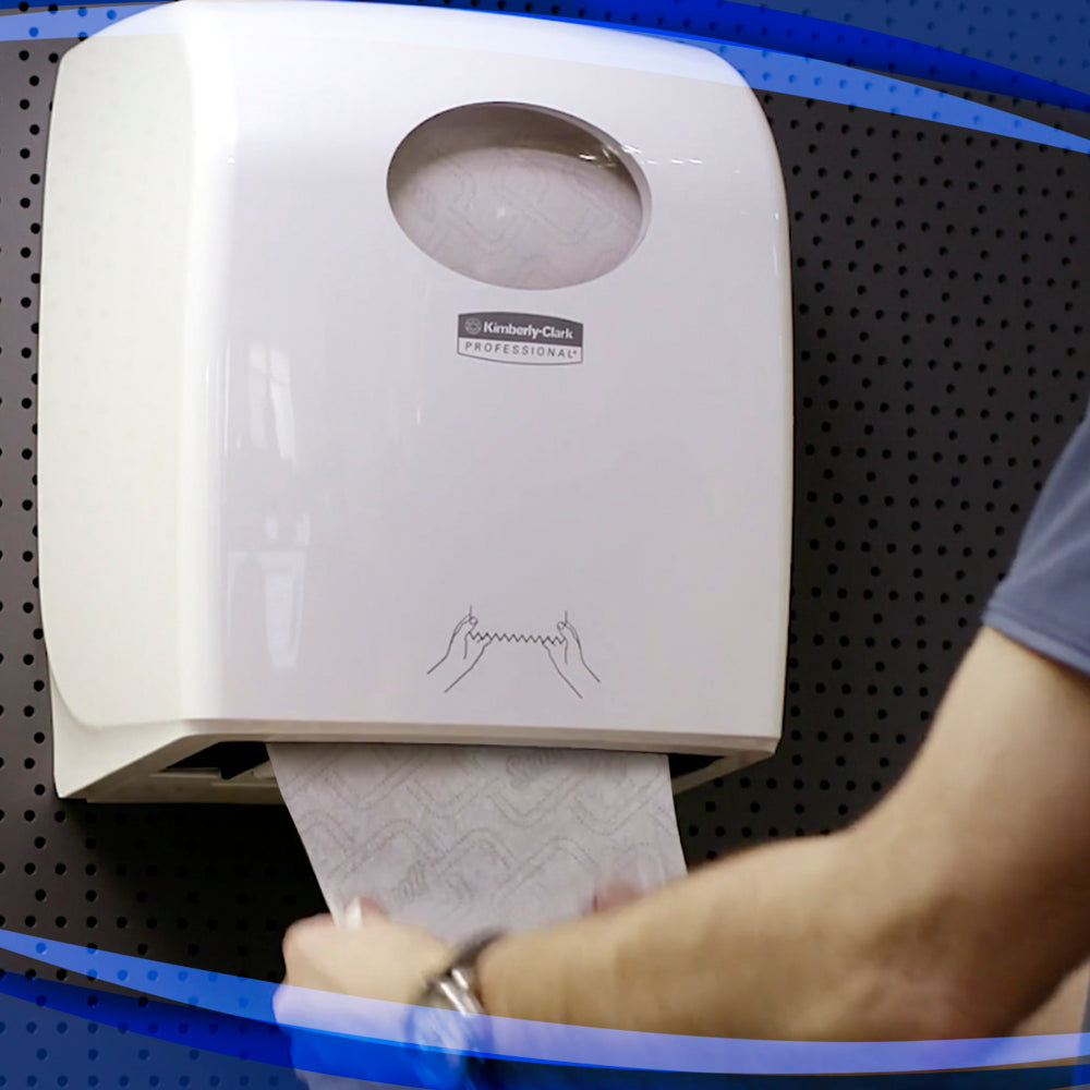 Eine Person zieht Papierhandtücher aus einem an der Wand montierten Aquarius™ Slimroll™ Rollenhandtuchspender - Weiß der Kimberly-Clark GmbH, der mit einer illustrierten Anleitung und einem modernen Design vor einer dunklen, gepunkteten Wand aufwartet.