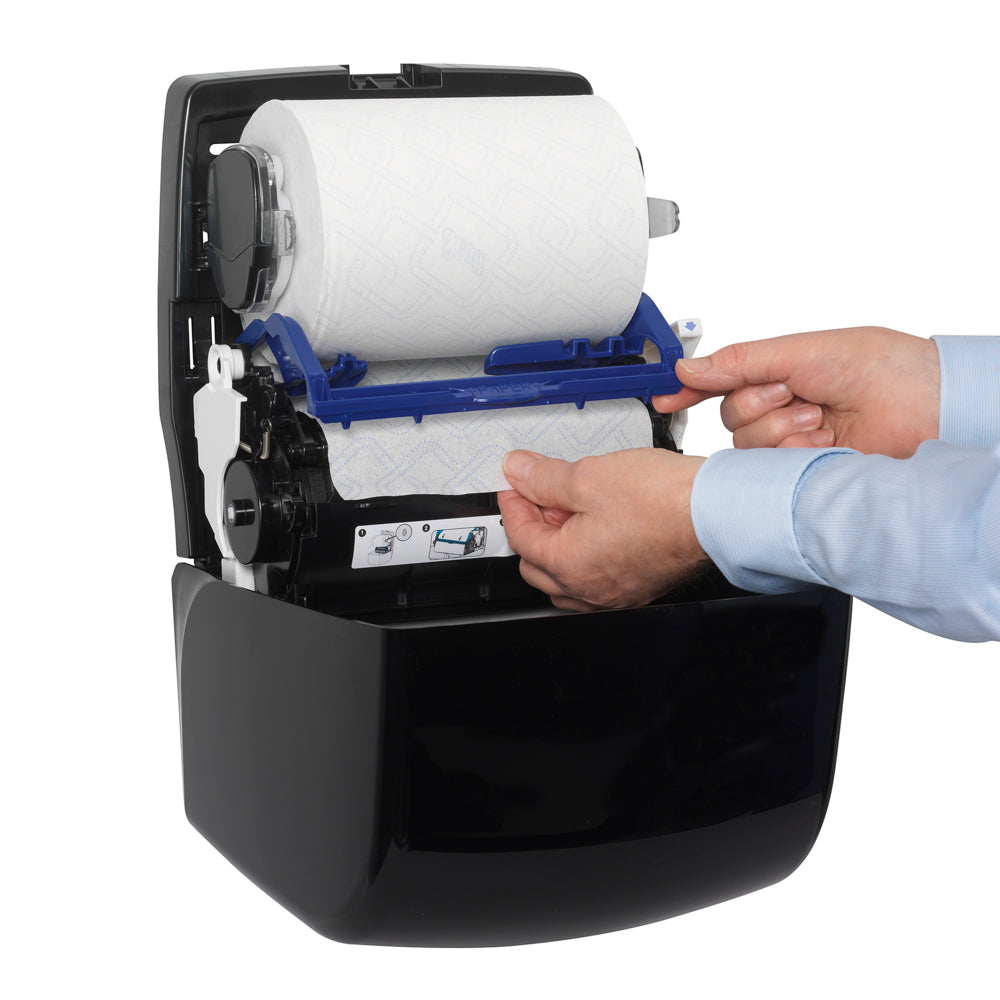 Eine Person in einem blauen Hemd legt eine Papierhandtuchrolle in einen Aquarius™ Slimroll™ Rollenhandtuchspender - Schwarz der Kimberly-Clark GmbH ein und fädelt das Papier sorgfältig ein, um es hygienisch zu spenden.