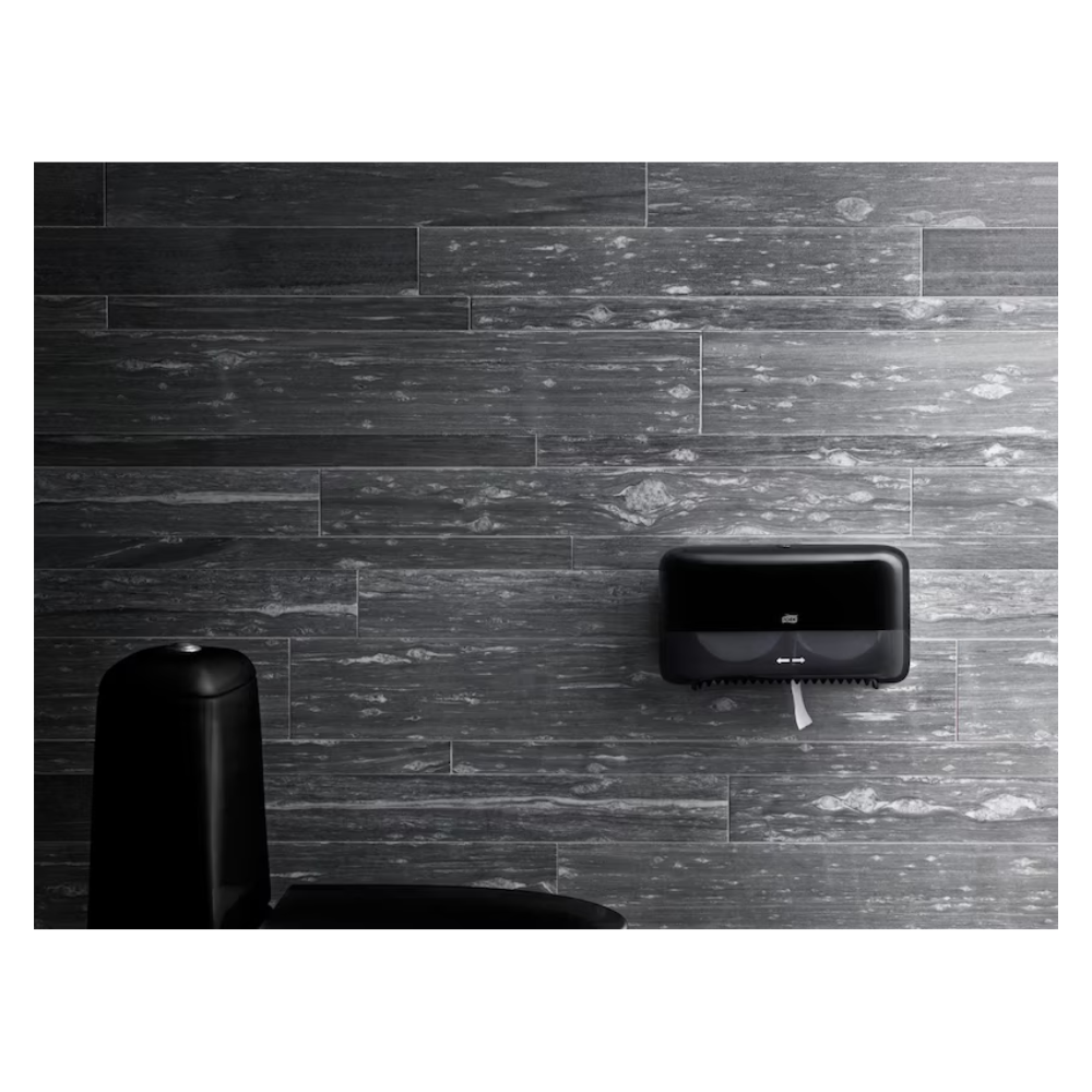 Ein modernes Badezimmer mit dunkelgrau strukturierten Wänden präsentiert einen hochwertigen, an der Wand montierten Tork-Papierhandtuchspender in Schwarz und gibt den Blick teilweise auf einen eleganten schwarzen Mülleimer im Vordergrund frei, wobei gleichzeitig ein umweltfreundliches Design beibehalten wird.