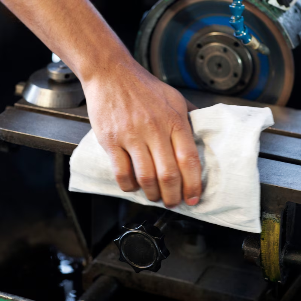 Eine Person wischt mit einer Rolle Tork 570137 Extra Starke Industrie Reinigungstücher W1 W2 W3 1-lagig eine Metalloberfläche einer Maschine ab. Teile der Maschine wie Räder und Knöpfe sind sichtbar, was die Wirksamkeit dieser wiederverwendbaren Tücher von TORK – Essity Professional Hygiene Germany GmbH bei der Aufrechterhaltung von Sauberkeit und Effizienz unterstreicht.