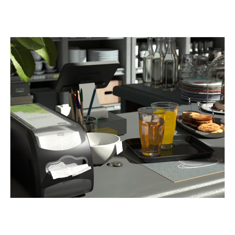 Auf einer Thekenszene in einem Café oder einer Küche wird neben der Kasse ein Tork Xpressnap Fit® 272901 Thekenspender für Servietten von TORK – Essity Professional Hygiene Germany GmbH präsentiert. Daneben stehen auf einem Tablett zwei Gläser Orangensaft und ein Stapel Kekse, während auf Regalen im Hintergrund Flaschen und Geschirr ausgestellt sind.