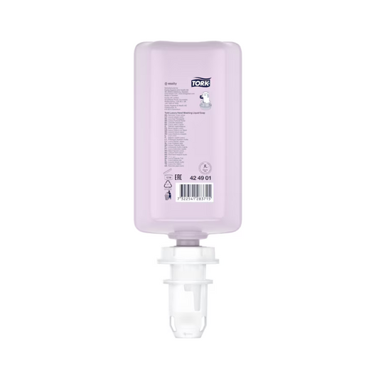 Eine rosa, rechteckige Flasche Tork luxuriöse Flüssigseife mit weißem Verschluss wird ausgestellt. Sie zeigt Produktdetails und einen Barcode und enthält luxuriöse Flüssigseife mit natürlichen Inhaltsstoffen, angereichert mit Magnolienextrakt. Diese Nachfüllung ist kopfüber positioniert, um sie einfach in einen Spender einzulegen, und ist Teil eines Sets der Marke TORK der Essity Professional Hygiene Germany GmbH.