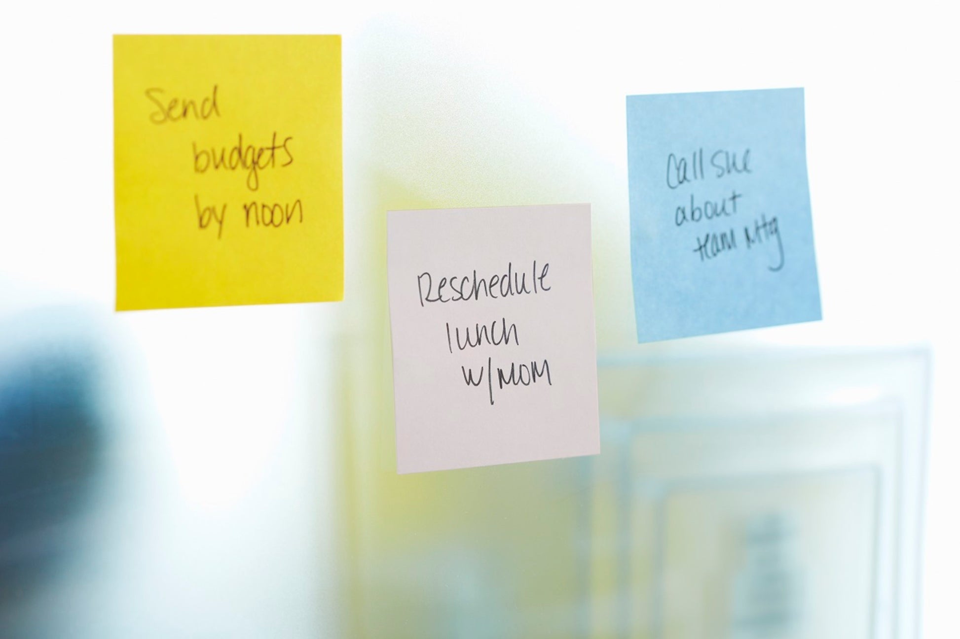 Drei Post-it® Super Sticky Notes Würfel von 3M Deutschland GmbH, gelb, 76 mm x 76 mm, befinden sich auf einer Glasfläche - gelb: "Budgets bis Mittag verschicken", lila: "Mittagessen mit Mama verschieben", blau: "Sue wegen Teambesprechung anrufen".