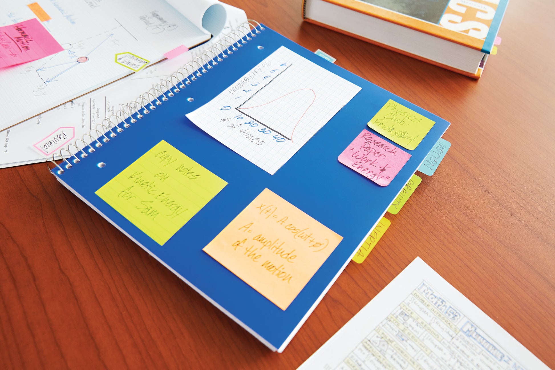 Ein blaues Spiralnotizbuch mit 3M Post-it® Notes in verschiedenen Neonfarben (38x51 mm, 3+1 Gratispackung, 100% PEFC) liegt auf einem Holztisch mit Schulbüchern und handschriftlichen Notizen.
