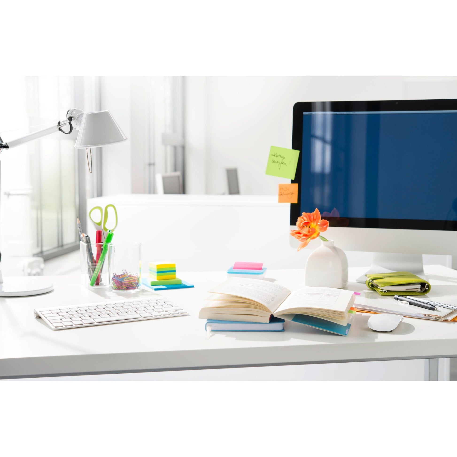Auf dem aufgeräumten Schreibtisch liegen ein aufgeschlagenes Buch, eine Tastatur, ein Monitor mit Post-it® Super Sticky Notes (76 mm x 76 mm, 90 Blatt/Block) von 3M Deutschland GmbH sowie Büroartikel wie Stifte, Scheren, Büroklammern und eine kleine Vase mit einer orangefarbenen Blume.