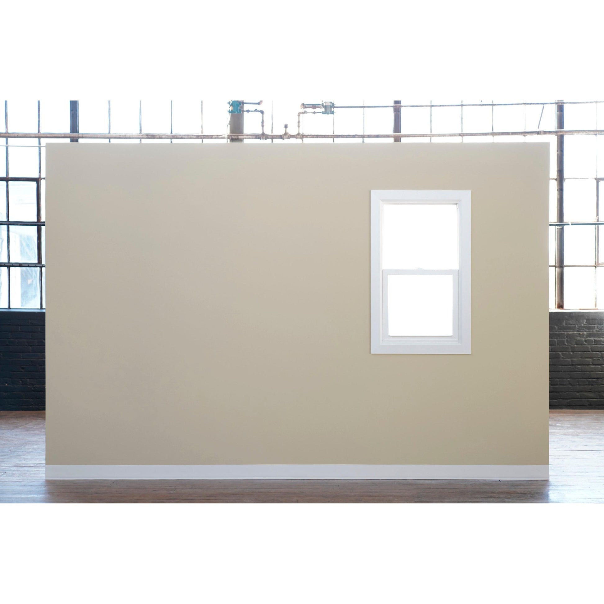 Eine beige Innenwand mit einem weiß gerahmten Fenster steht auf einem Holzboden vor Industriefenstern. Zum präzisen Streichen verwenden Sie Scotch® Classic Abdeckband, 36 mm x 50 m von 3M Deutschland GmbH-70% PEFC zertifiziert (1 Rolle pro Packung).