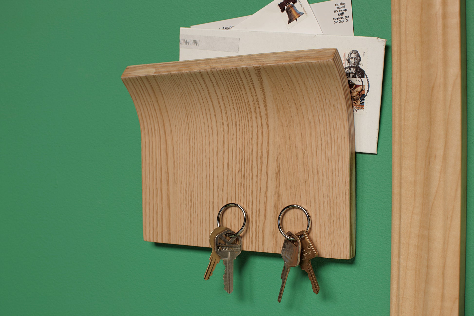 Ein hölzerner Wandbriefkasten mit Haken für Schlüssel wird mit dem Scotch-FIX™ Doppelseitigen Innenmontageband der 3M Deutschland GmbH an einer grünen Wand befestigt.