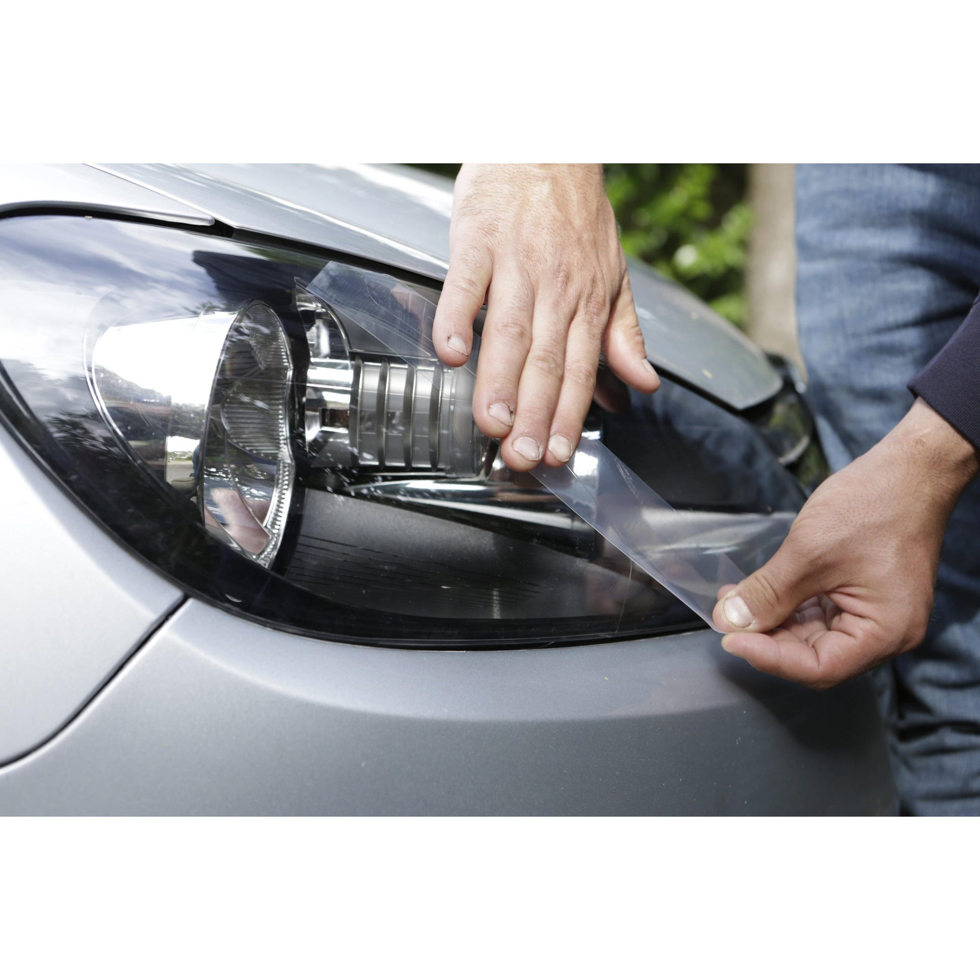 Eine Person verwendet 3M Deutschland GmbH Scotch® Extremium™ INVISIBLE Hochleistungs-Klebeband (20 m x 48 mm), um eine schützende Klarsichtfolie auf einem silbernen Autoscheinwerfer zu befestigen, wobei sie die Folie von Hand über die Oberfläche streicht.