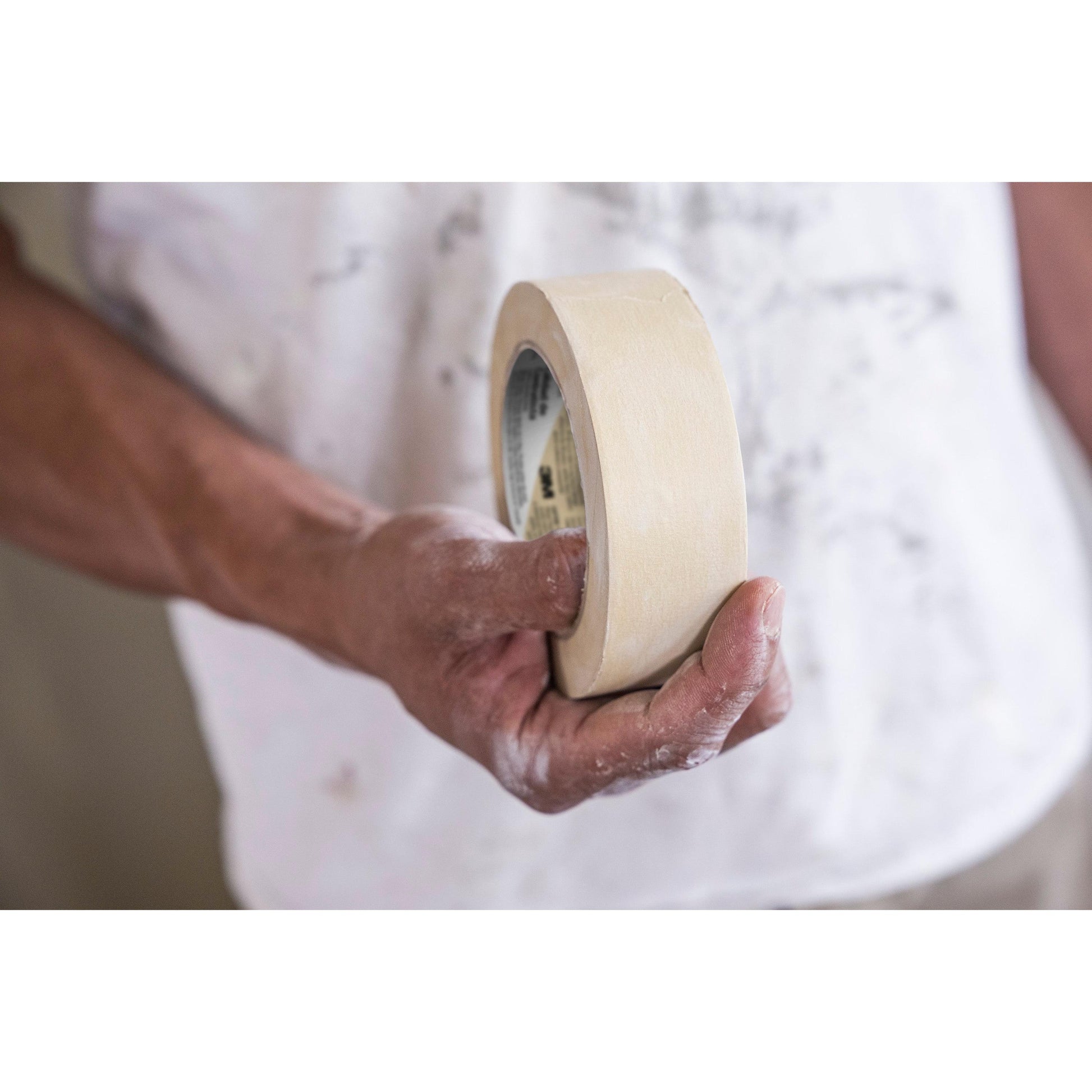 Eine Person im weißen Hemd, die Finger mit Farbe bestäubt, hält eine Rolle Scotch® Classic Abdeckband (24 mm x 50 m) der 3M Deutschland GmbH - verpackt als 1 Rolle/Packung und hergestellt aus 70% PEFC-zertifiziertem Material.