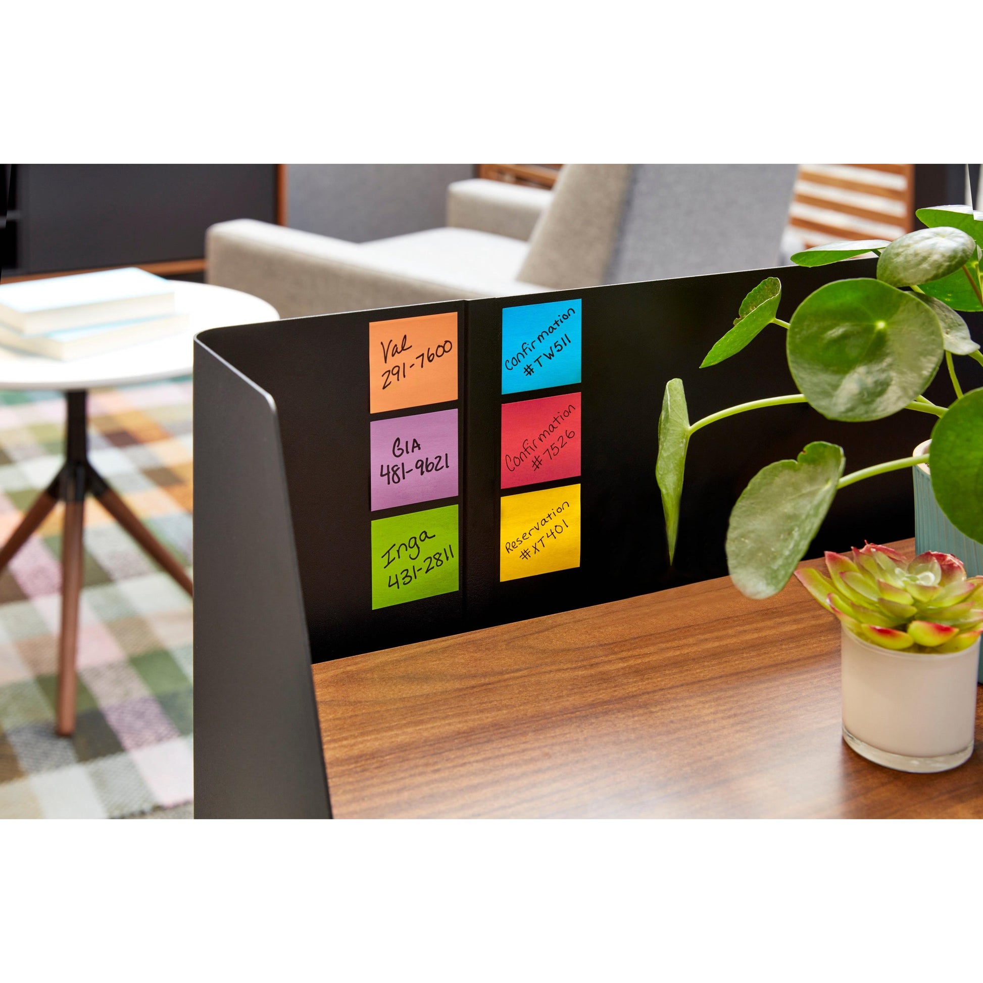 Eine Nahaufnahme einer Schreibtischunterteilung mit sechs bunten Post-it® Super Sticky Notes (76 mm x 76 mm, 90 Blatt/Block, 100% PEFC) von 3M Deutschland GmbH, die Details zeigt. Eine Grünpflanze und unscharfe Büromöbel vervollständigen die Szene.
