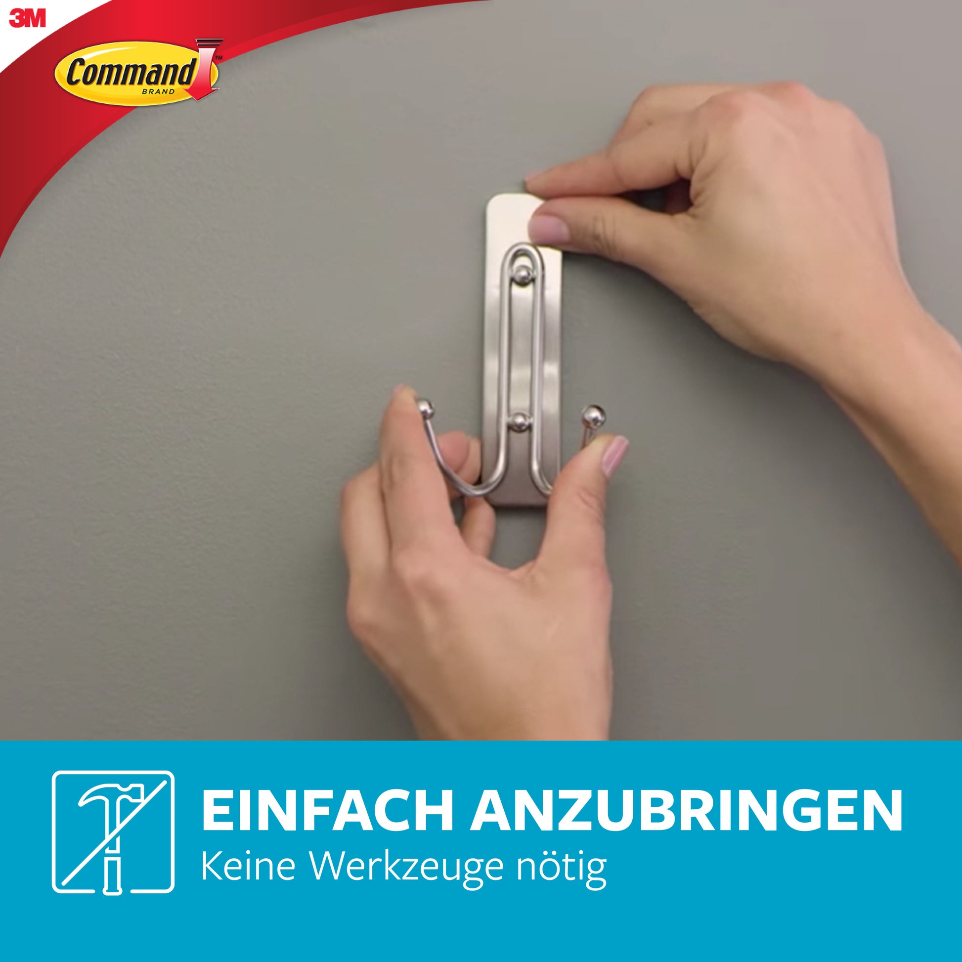 Eine Person bringt den 3M Command™ Großer Badezimmer-Doppelhaken Nickel satiniert an einer grauen Wand mit großen Strips an. Der deutsche Text lautet: "Einfach anbringen. Keine Werkzeuge nötig." Das Logo der 3M Deutschland GmbH ist sichtbar.