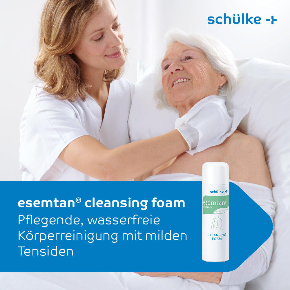 Eine Pflegefachkraft trägt sanft Schülke Esemtan® Reinigungsschaum auf den Hals einer älteren Frau auf und strahlt so Geborgenheit und Pflege aus. Die 500-ml-Flasche und der Markenname Schülke & Mayr GmbH sind gut sichtbar angebracht.