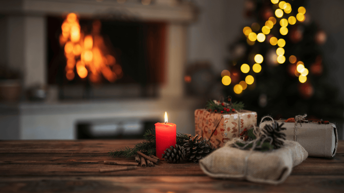 Weihnachtliche Szene mit brennender Kerze, Geschenken und Tannenzapfen auf Holztisch vor Kamin und Weihnachtsbaum