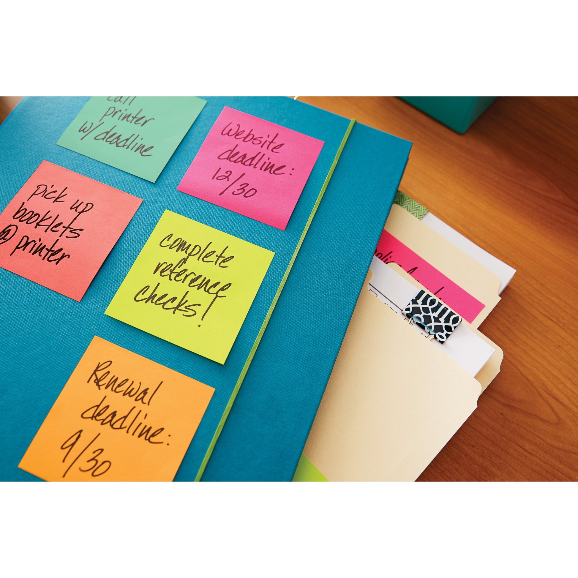 Eine blaue Mappe mit Post-it® Zetteln der 3M Deutschland GmbH (76 mm x 76 mm, 100 Blatt/Block, 100% PEFC), auf denen Aufgaben und Termine vermerkt sind, liegt auf einem Holztisch neben geordneten Aktenordnern mit Registerkarten.