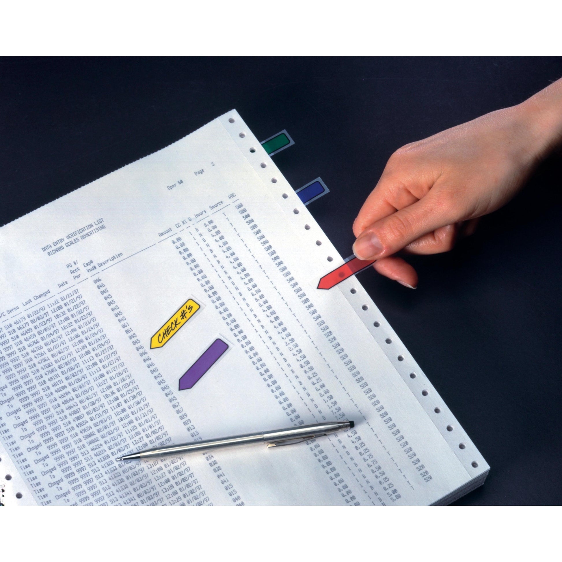 Eine Hand legt einen roten Post-it® Index Pfeil (11,9 mm x 43,2 mm) von 3M Deutschland GmbH auf Computerausdruckpapier. Andere farbige Haftstreifen und ein Stift liegen daneben auf der dunklen Fläche. Packung: 100 Haftstreifen/Spender.