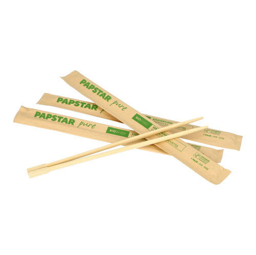 Drei PAPSTAR 50 Paar Essstäbchen „pure“ (23 cm) der PAPSTAR GmbH werden mit einzelnen Hüllen mit der Aufschrift „PAPSTAR pure“ gezeigt. Ein Paar wird zur Hygienedemonstration aus der Hülle genommen und diagonal hingelegt.