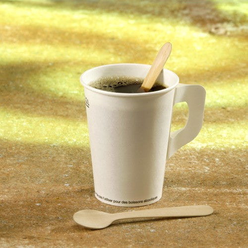 Ein weißer Pappbecher mit Kaffeefüllung steht auf einer strukturierten Unterlage. Im Inneren befindet sich ein PAPSTAR 100 Kaffeelöffel, Holz „pure“ 11 cm der PAPSTAR GmbH, ein weiterer steht davor.
