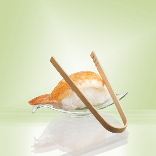 Ein Garnelen-Nigiri liegt auf einer Glasschale, daneben PAPSTAR 10 Fingerfood-Zangen, Bambus 10 cm (Beutel, 10 Stück) der PAPSTAR GmbH, alles vor einem hellgrünen Farbverlauf als nachhaltige Servierlösung.