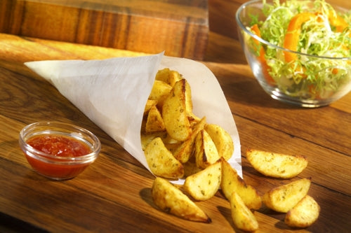 Eine PAPSTAR 1000 Spitztüte, Pergament-Ersatz, fettdichte Papiertüte der PAPSTAR GmbH, gefüllt mit gewürzten Kartoffelspalten, steht auf einer Holzfläche neben roter Dip-Sauce und einem grünen Salat mit Orangenscheiben im Hintergrund.