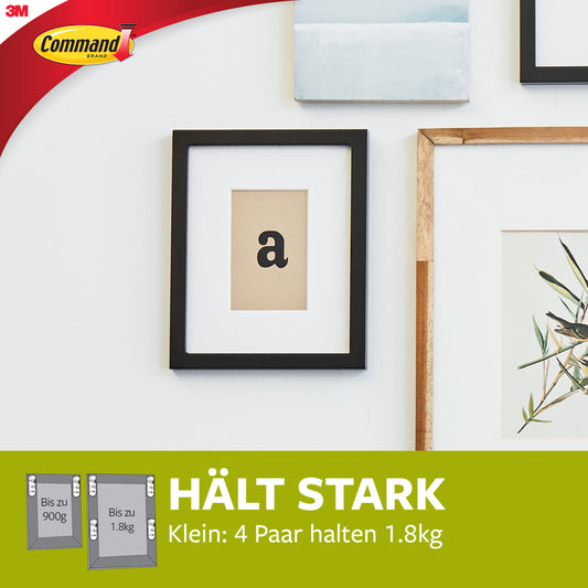Ein schwarz gerahmter Druck mit dem Buchstaben "a" hängt an einer weißen Wand, gesichert durch 3M Deutschland GmbH Kleine weiße Command™ Bilder-Montage Strips S 17202. Ein grünes Banner darunter zeigt das Command-Branding und deutsche Informationen zu Gewichtsgrenzen.