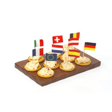 Ein Holztablett enthält sieben Cracker, jeweils mit einem Aufstrich und gekrönt mit PAPSTAR Deko-Picker 8 cm "Nationen" (verschiedene Länder & EU). Perfekt als Tischdekoration für Feiern und Events. Marke: PAPSTAR GmbH.