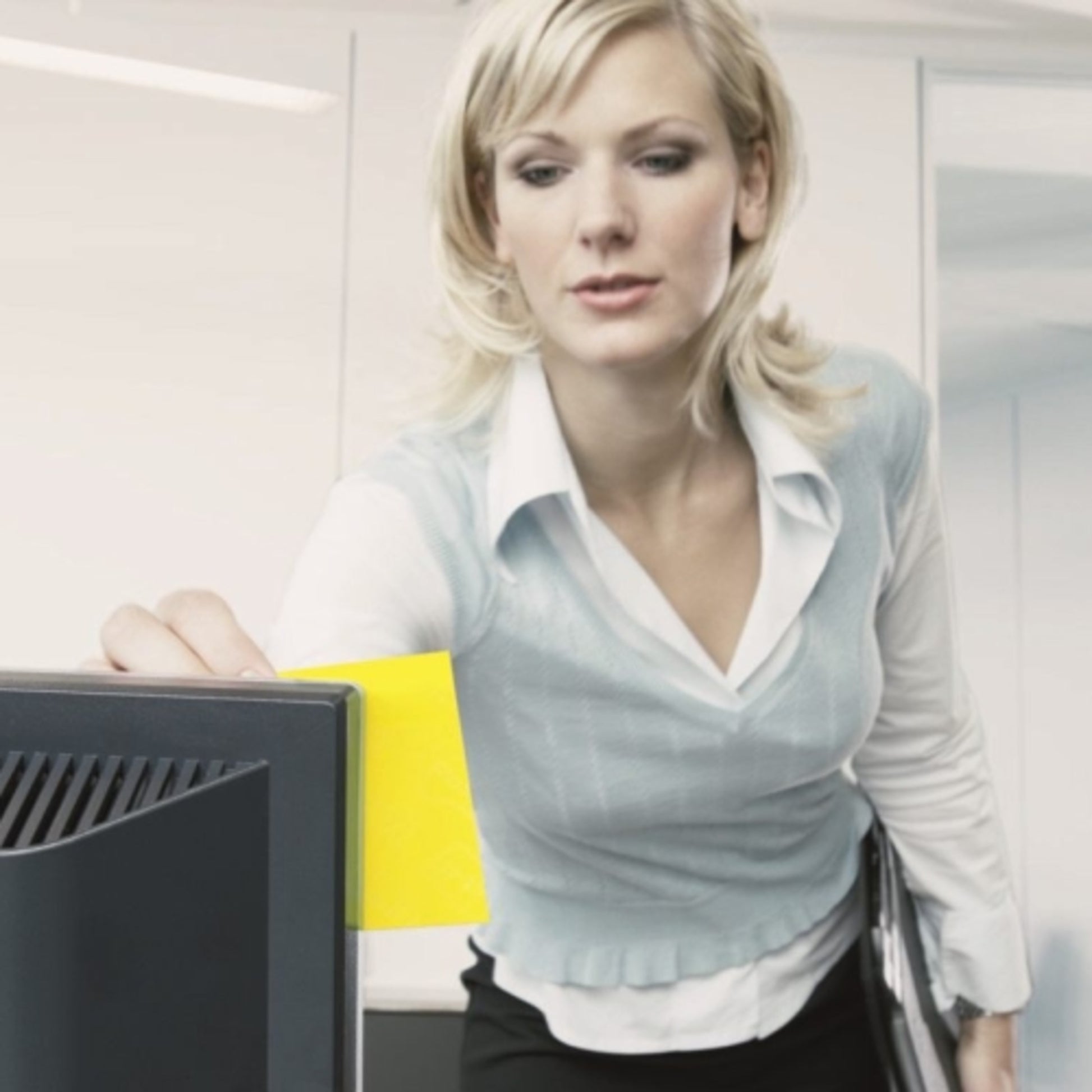 In einem Büro klebt eine Frau im Business-Outfit einen 3M Post-it® Notes Würfel 636-B (Gelb, 76x76 mm, 450 Blatt, PEFC-zertifiziert) auf ihren Monitor, während sie Dokumente hält.