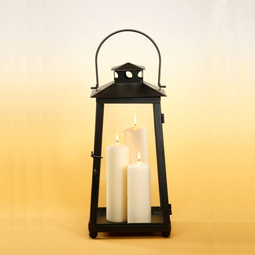Eine schwarze Metalllaterne mit Griff enthält drei brennende Starpak 3 Kamin- und Laternenkerzen Ø 70 mm Elfenbein (Packung, 3 Stück), vor einem Hintergrund mit Farbverlauf von Hellgelb unten nach Blassgelb oben.