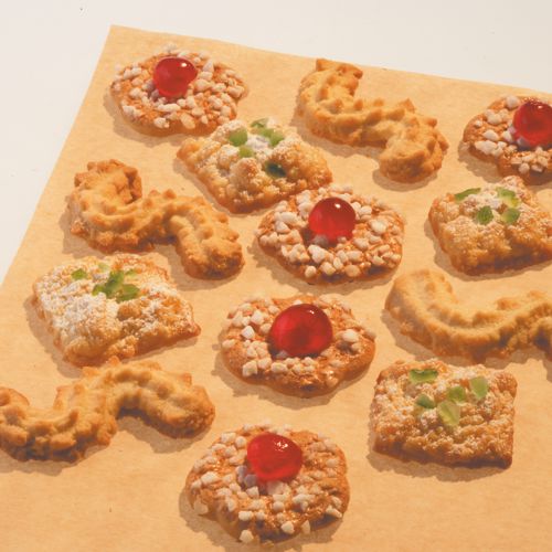 Zwölf verschiedene Butterkekse – teils mit Nüssen, roten Kirschen oder grünen kandierten Früchten – sind in Reihen auf einem Bogen PAPSTAR Backpapier 38 cm Breite der PAPSTAR GmbH mit praktischer Antihaft-Oberfläche angeordnet.