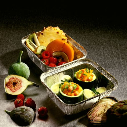 Zwei Starpak 25 Alu Schalen mit PP-beschichteten Deckeln sind mit frischem Obst wie Kiwi, Ananas, Feigen, Beeren und Gemüse wie Zucchini und Melone auf einer grauen Oberfläche gefüllt - ideal für Catering oder zum Mitnehmen.
