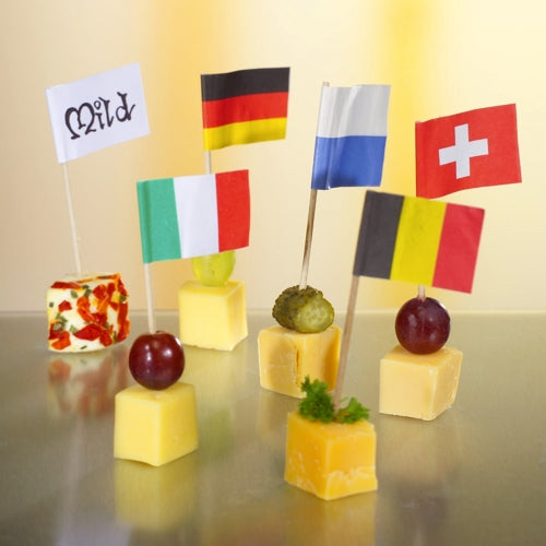 Six cheese cubes, each topped with an 8 cm large white deco-picker flag from PAPSTAR GmbH labeled "Mild", Germany, France, Switzerland, Italy, and Belgium; garnished with grapes or olives for an elegant presentation on a reflective tray.