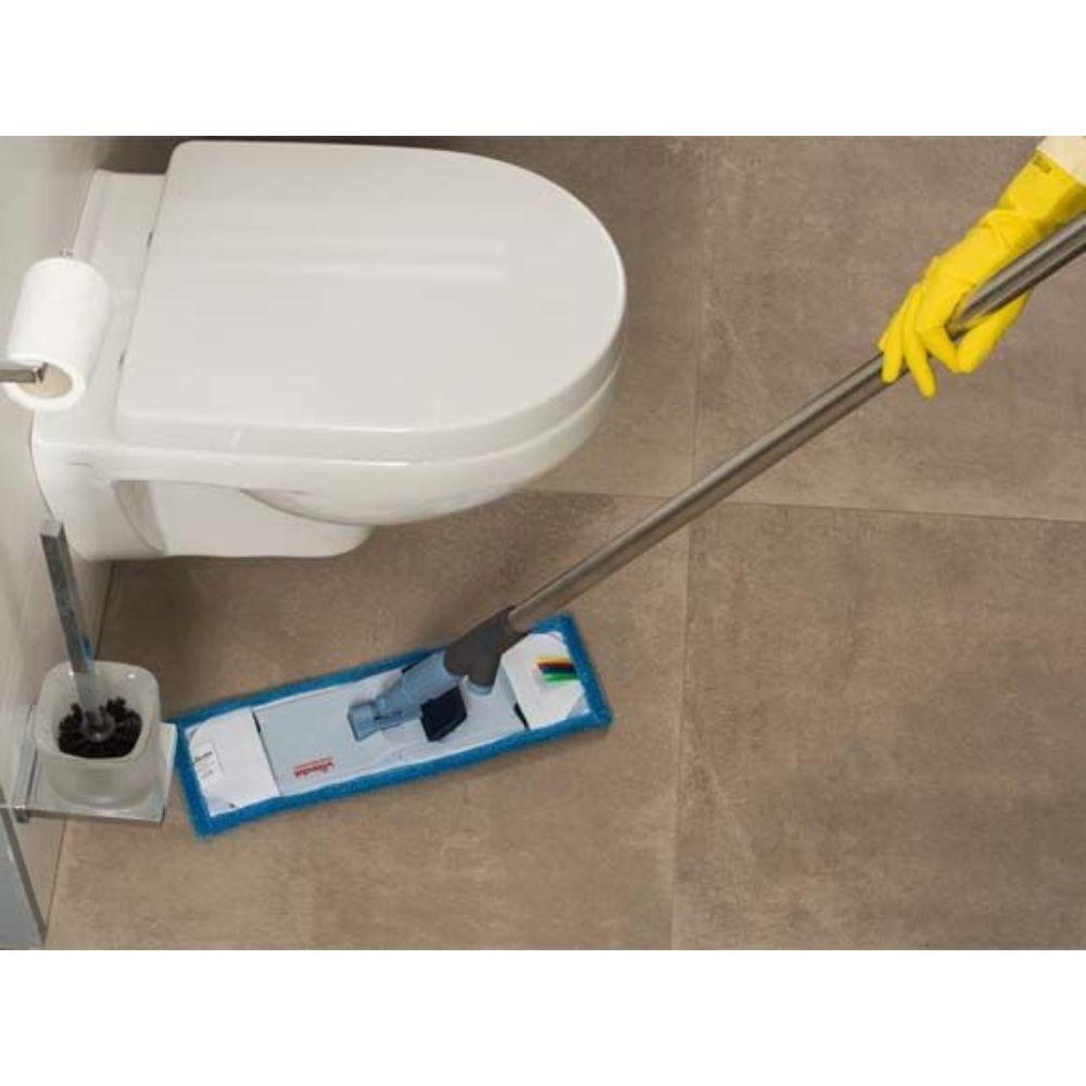 Eine Person mit gelben Handschuhen wischt effizient den gefliesten Badezimmerboden neben einer weißen Toilette mit dem Vileda Professional SprayPro Edelstahl Mopphalter der Vileda GmbH, der mit einem blau umrandeten Pad ausgestattet ist. In der Nähe befindet sich ein Halter, in dem die Toilettenbürste aufbewahrt wird.