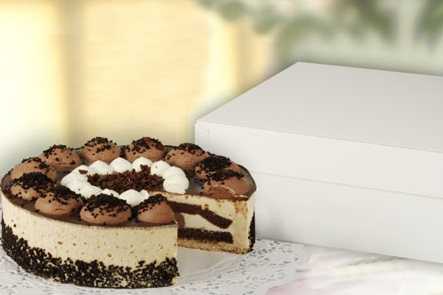 Eine runde Torte mit Schokoladen- und Cremeschichten liegt auf einem Spitzentuch neben einem geschlossenen PAPSTAR 10 Tortenkartons mit Deckel, Pappe eckig weiß von PAPSTAR GmbH; eine Scheibe ist herausgenommen, so dass die Schokolade und die Creme im Inneren sichtbar werden.