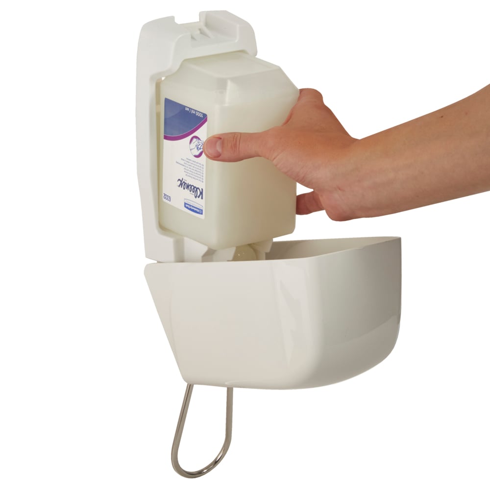 Eine Hand setzt eine 1 Ltr Aquarius™ Spender für Waschlotionen Kassette von Kimberly-Clark GmbH in einen weißen, wandmontierten Spender mit gewölbter Vorderseite und Metallstütze darunter ein.