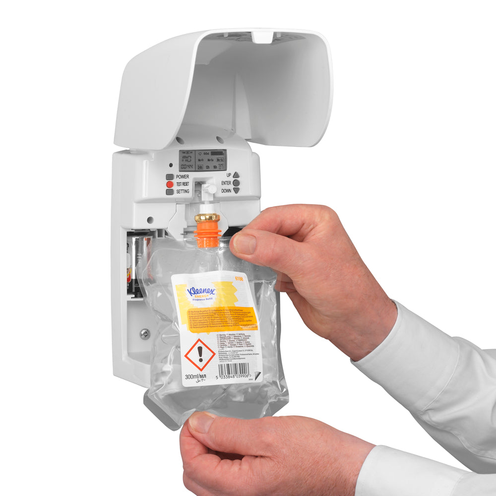 Eine Person führt eine Kleenex® Duft Energy Nachfüllpackung (300 ml, transparent) der Kimberly-Clark GmbH in einen weißen Wandspender ein und bereitet damit das Raumduft-System vor. Die Kartusche ist mit einem Gefahrenetikett versehen und es sind sichtbare Kontrollen vorhanden.