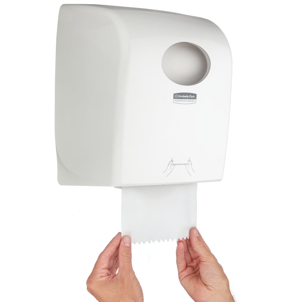 Eine Person zieht ein Papierhandtuch aus einem Kimberly-Clark GmbH Aquarius™ Rollenhandtuchspender - Weiß mit kreisrunder Öffnung und einer instruktiven Grafik - ideal für öffentliche Bereiche.