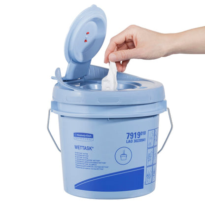 A hand pulls a WypAll® Wettask™ PowerClean wipe from a light blue container by Kimberly-Clark GmbH with a flip-top lid. The box contains 6 rolls with 60 sheets each and is printed on the side with product information and illustrations.