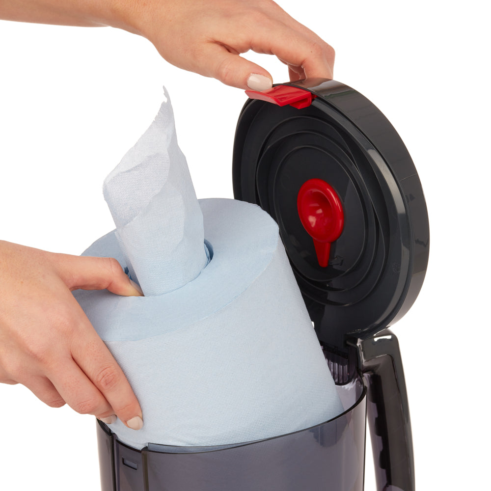 Eine Person legt eine große blaue Papierhandtuchrolle in einen schwarzen WypAll® Reach™ Centrefeed Dispenser der Kimberly-Clark GmbH ein und öffnet den Klappdeckel, um den roten Auslösemechanismus für die hygienische Papierausgabe freizugeben.