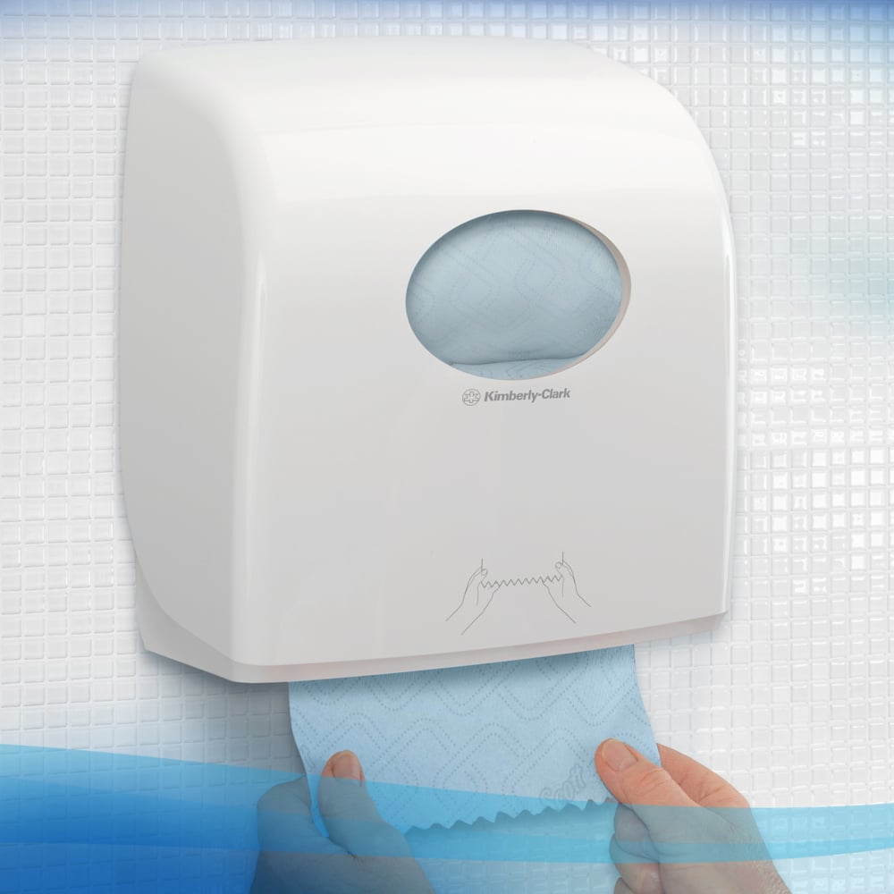 Ein weißer Spender der Kimberly-Clark GmbH für Scott® Essential™ Slimroll™ Handtücher (190,00 m x 19,80 cm) ist an der Wand montiert, mit einer Hand, die ein blaues Tuch herauszieht, sichtbar im runden Fenster für umweltfreundliche Händetrocknung.