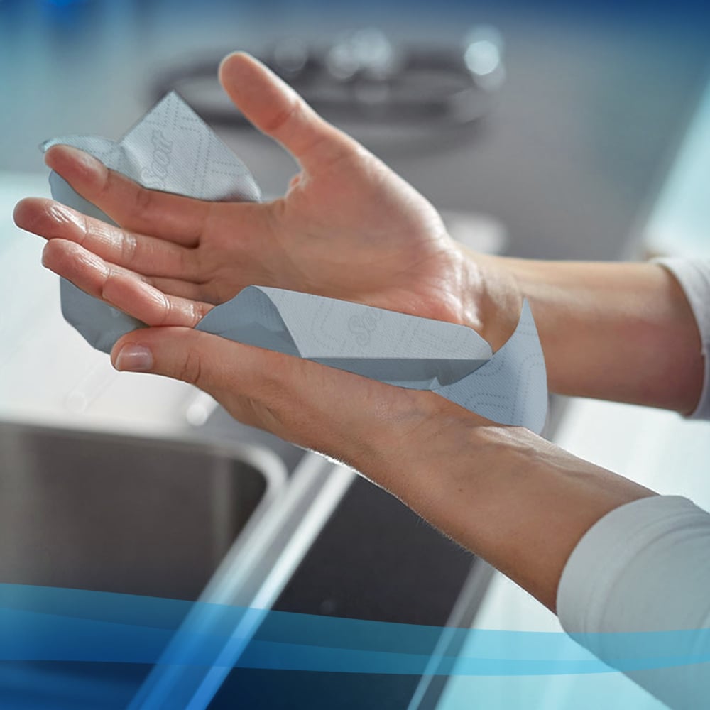 Eine Person trocknet ihre Hände mit Scott® Essential™ Slimroll™ Handtüchern (190,00 m x 19,80 cm) von Kimberly-Clark GmbH über einem Waschbecken in einer modernen Küche - für umweltfreundliche Händetrocknung.