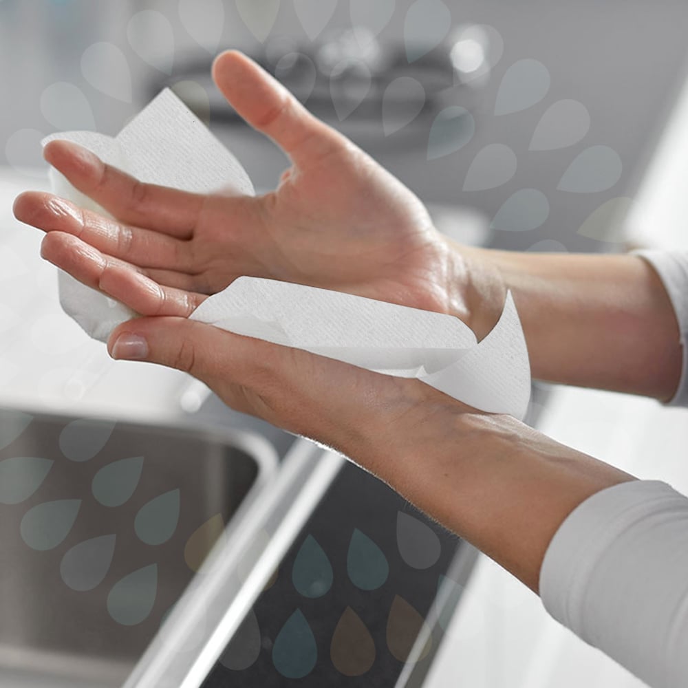 Eine Person trocknet ihre Hände über einem Spülbecken mit Kleenex® Falthandtüchern - Weiß /Groß (15 Clips x 124 Blatt | Karton) von Kimberly-Clark GmbH, wobei beide Hände und ein Teil des Spülbeckens im Hintergrund zu sehen sind.