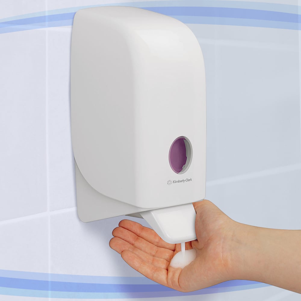 A person dispenses foam soap from a white Aquarius™ dispenser for wash lotions - cassette / 1 Ltr from Kimberly-Clark GmbH onto their hand in a tiled bathroom.