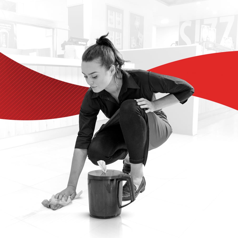 Eine Frau in dunkler Kleidung reinigt einen Fliesenboden mit einem WypAll® Reach™ Papierwischtuch für Lebensmittel & Hygiene - Zentralentnahme von Kimberly-Clark GmbH. In der Nähe steht ein Putzeimer; der schwarz-weiße Hintergrund ist mit einer kräftigen roten Welle versehen, die die Hygiene hervorhebt.