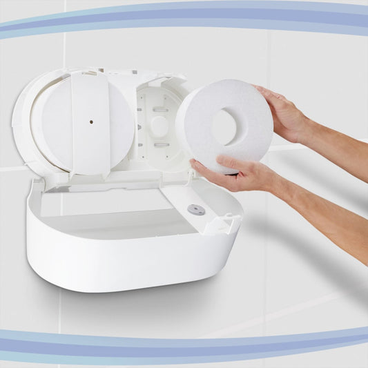 Eine Person legt eine große Rolle Scott® Control™ Toilettenpapier - Zentralentnahme von Kimberly-Clark GmbH in einen weißen Wandspender in einer gefliesten Toilette ein; das geöffnete Gerät gibt das Fach und die Spindel frei - ideal für professionelle Umgebungen.