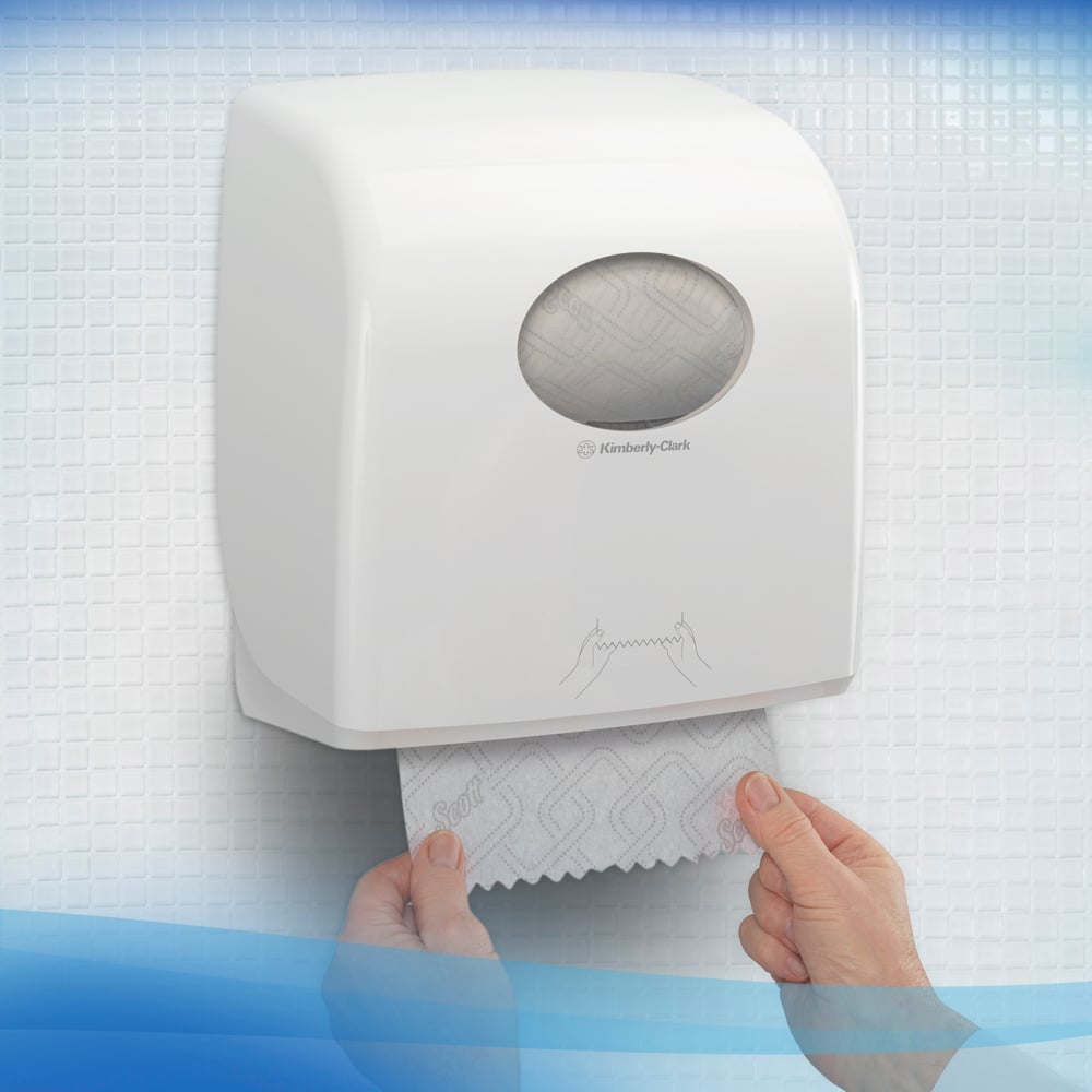 Eine Person zieht Scott® CONTROL EXTRA STRONG Handtücher aus einem an der Wand montierten, weißen Spender der Kimberly-Clark GmbH, der auf weißen, strukturierten Fliesen steht. Auf der Vorderseite des Rollen-Handtuchspenders ist eine einfache Gebrauchsanweisung abgebildet.