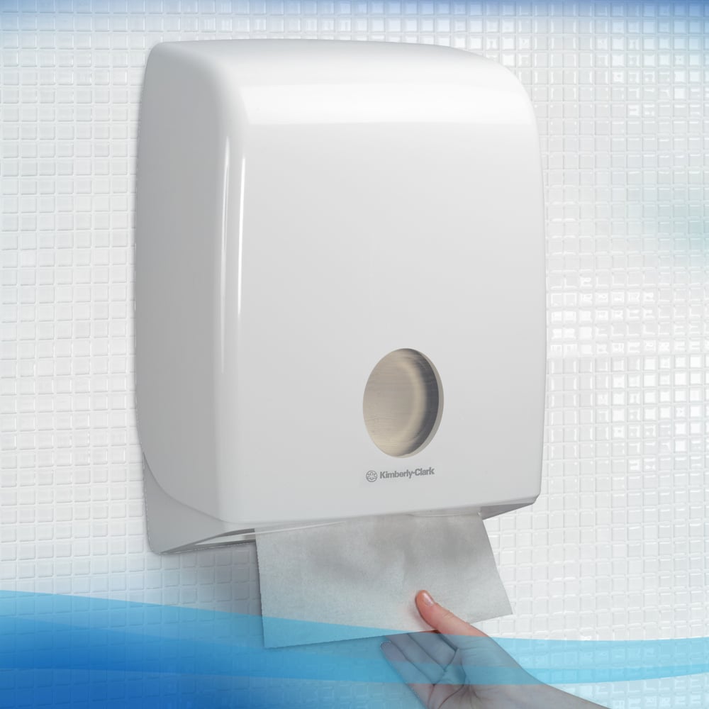 A hand pulls a Scott® Control™ Interfold Hand Towel from a white Kimberly-Clark dispenser in a tiled washroom, ensuring hygienic hand drying.