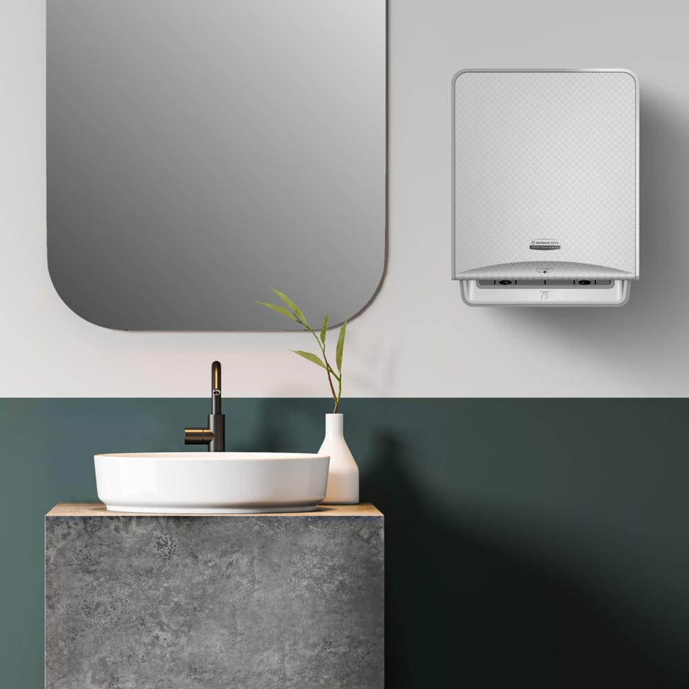 A modern bathroom with a square mirror, a vessel sink on a concrete countertop, a black faucet, a white vase with greenery, and a wall-mounted dispenser for hygienic hand drying with Kleenex® roll towels from Kimberly-Clark.