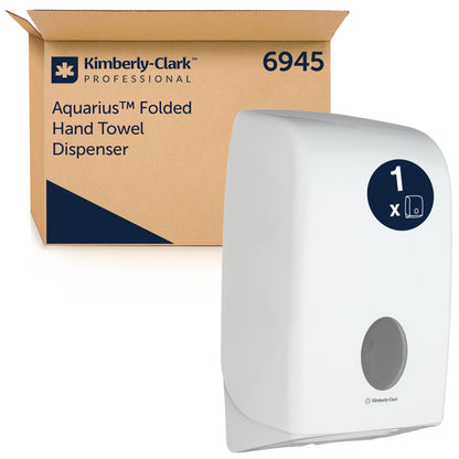A white Aquarius™ dispenser for folded towels from Kimberly-Clark GmbH stands next to a brown box labeled "6945". The dispenser has a round window that ensures hygienic towel dispensing. 1 dispenser per carton.