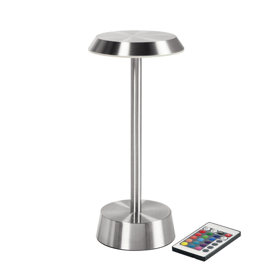 Die kabellose LED-Lampe NOUR von Duni GmbH in Silber steht mit rundem Sockel und Schirm aufrecht, daneben liegt eine kleine Fernbedienung mit bunten Tasten.
